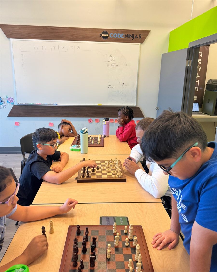 Ninjas playing a chess tournament at long tables under the Code Ninjas sign.